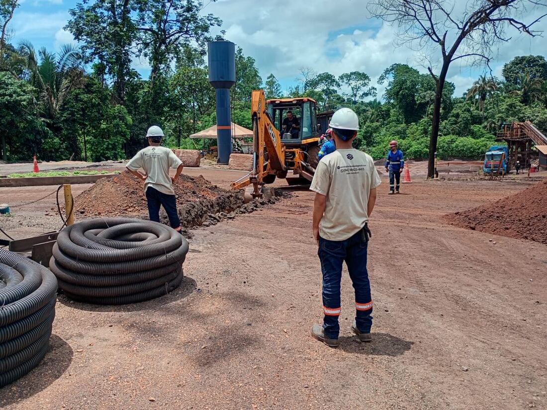 Equipe da S.Saraiva acompanhando escavação de vala com retroescavadeira, ao lado de bobinas de tubo corrugado