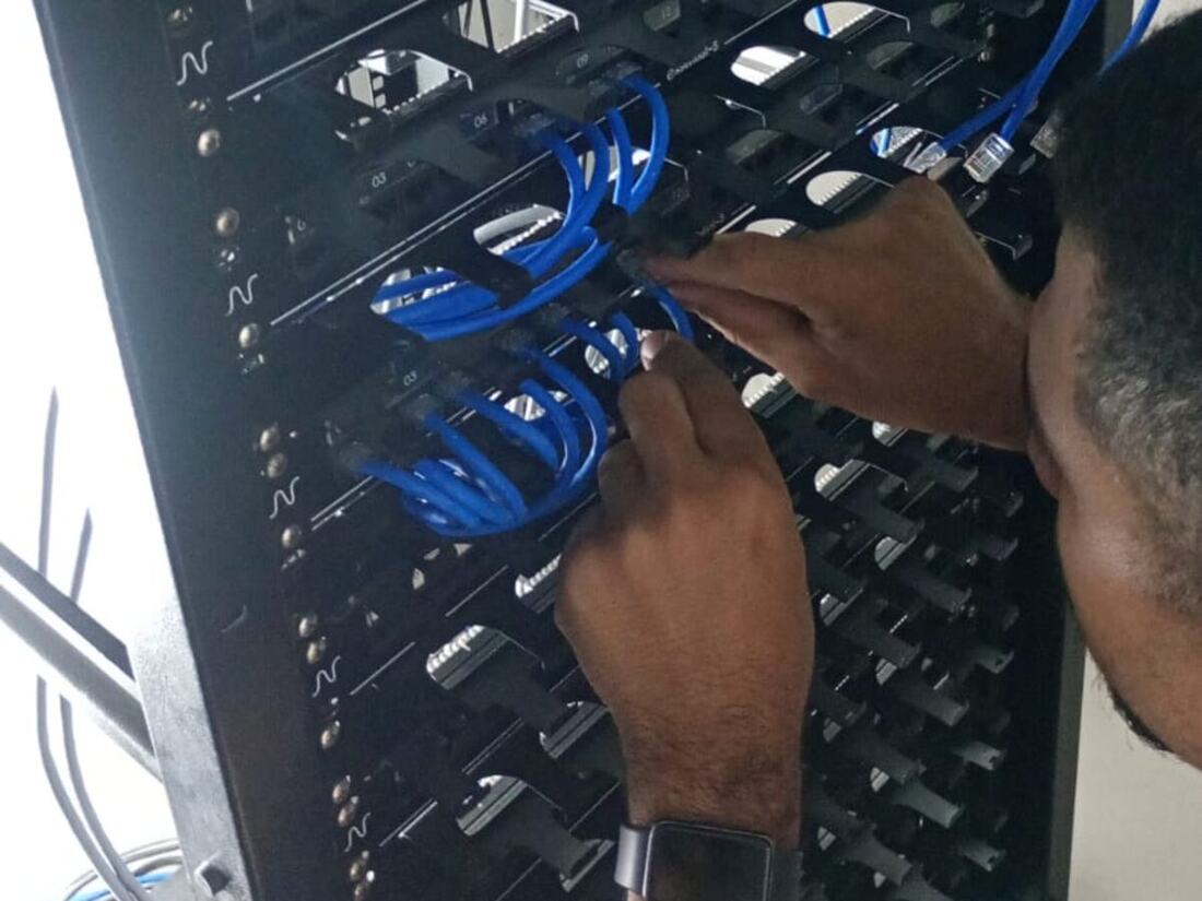 Técnico conectando cabos azuis em patch panel dentro de rack de rede